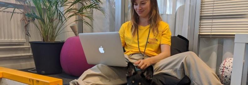 Salla-Mari smiling and sitting with a laptop and a puppy in her feet.